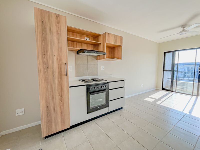 Modern kitchen featuring built-in cabinetry, oven, hob, and extractor fan, with tiled flooring and access to a balcony through a sliding glass door.