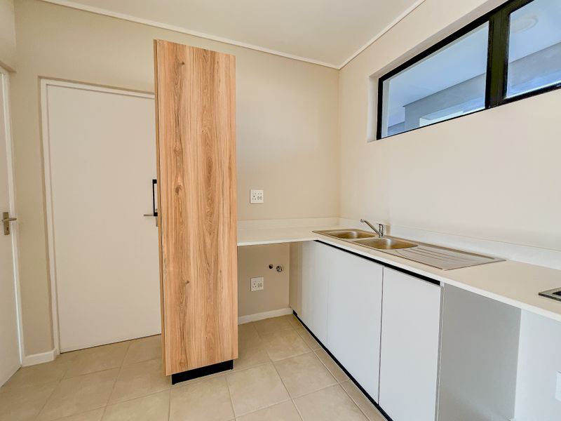 A clean and modern laundry room featuring a stainless steel double sink, stone countertops, and ample built-in cabinetry for storage and utility needs.