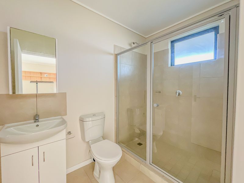 A clean and functional bathroom featuring a vanity with basin, a toilet, and a glass-enclosed shower with tiled walls.
