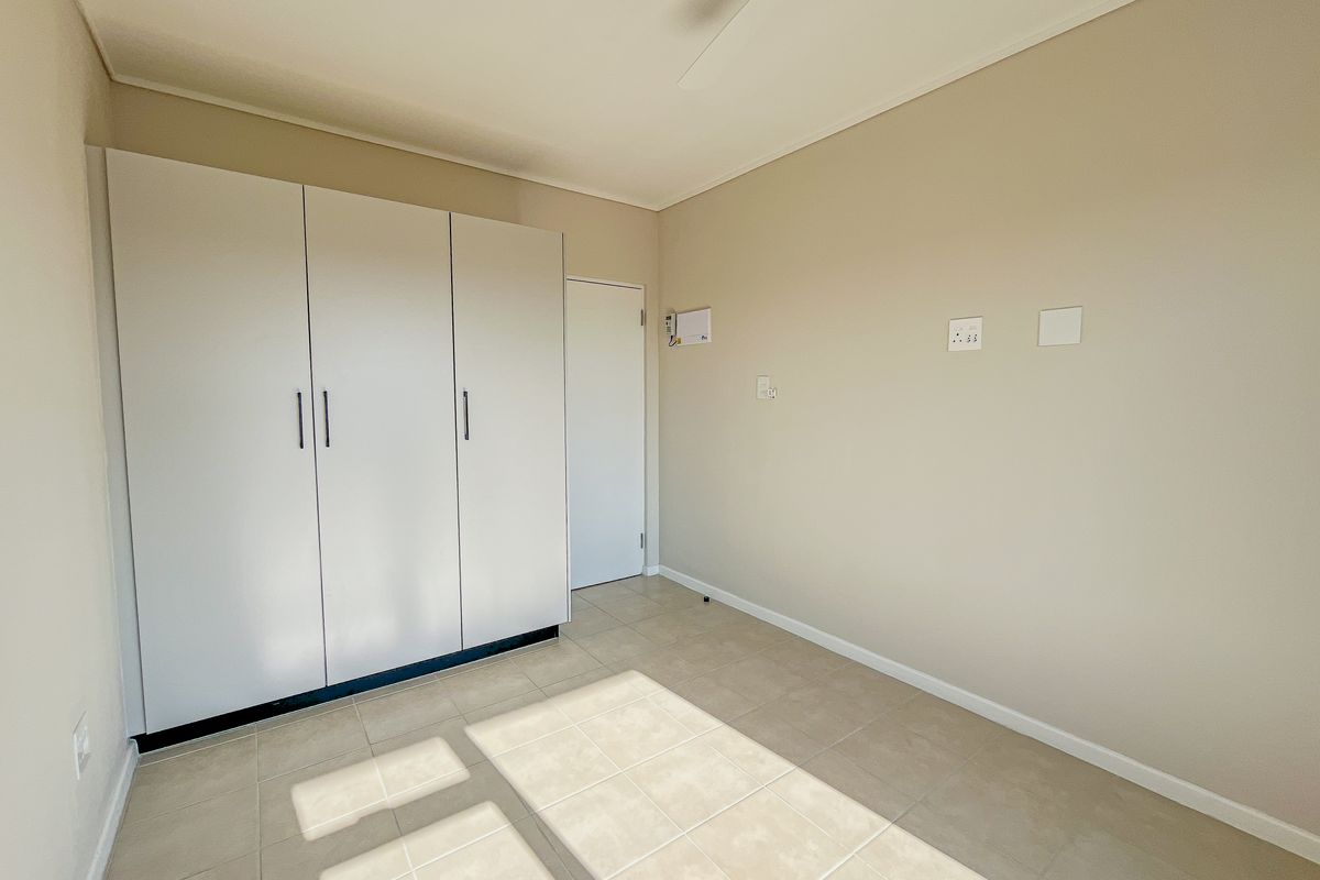 A bright, empty bedroom featuring neutral tiled flooring, a built-in wardrobe, and a ceiling fan, offering a clean and versatile living space.