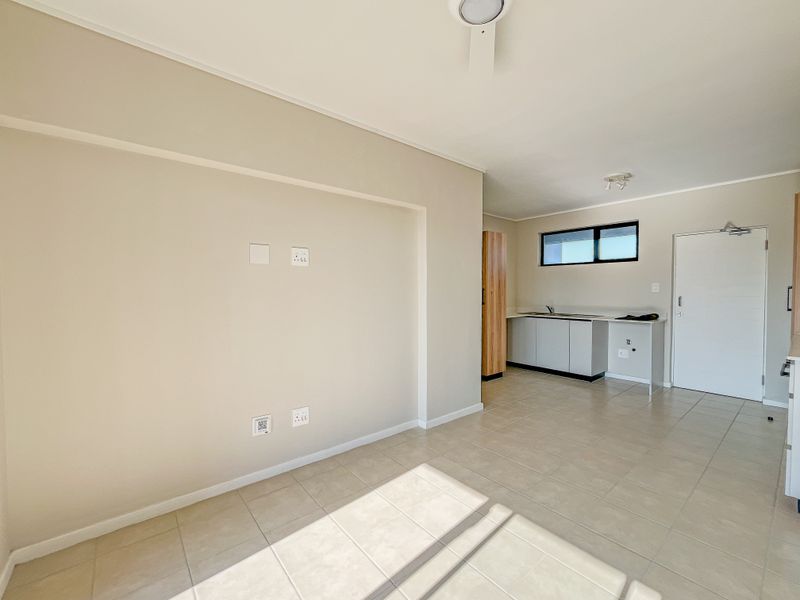 An open-plan living and kitchen area featuring neutral tiled flooring, built-in cabinetry, and a ceiling fan in a clean, vacant space.