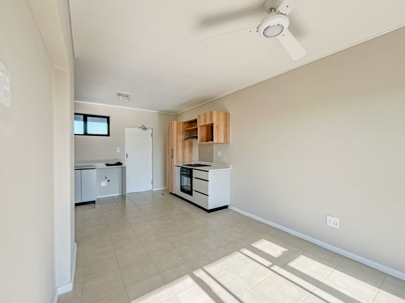 An open-plan living and kitchen area featuring tiled flooring, built-in cabinetry with integrated oven and hob, and a ceiling fan.