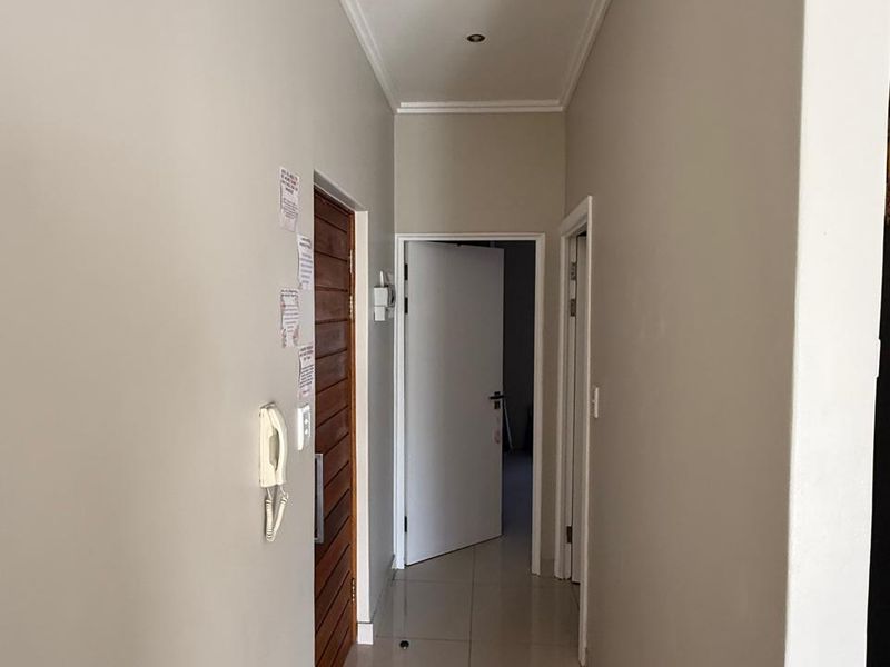 A clean and well-maintained hallway featuring neutral tiled flooring, recessed downlighting, and decorative cornicing, providing access to multiple rooms within the apartment.