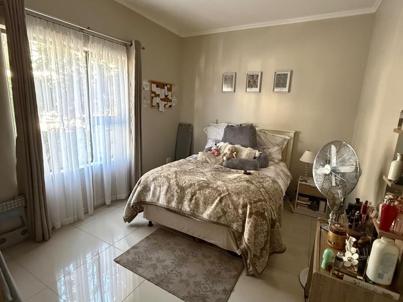 A well-lit bedroom featuring neutral wall tones, large windows with sheer curtains, and polished tiled flooring throughout.