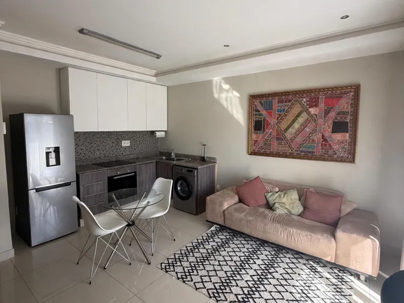 Open-plan living area featuring a modern kitchen with built-in cabinetry, integrated appliances, and tiled flooring throughout.