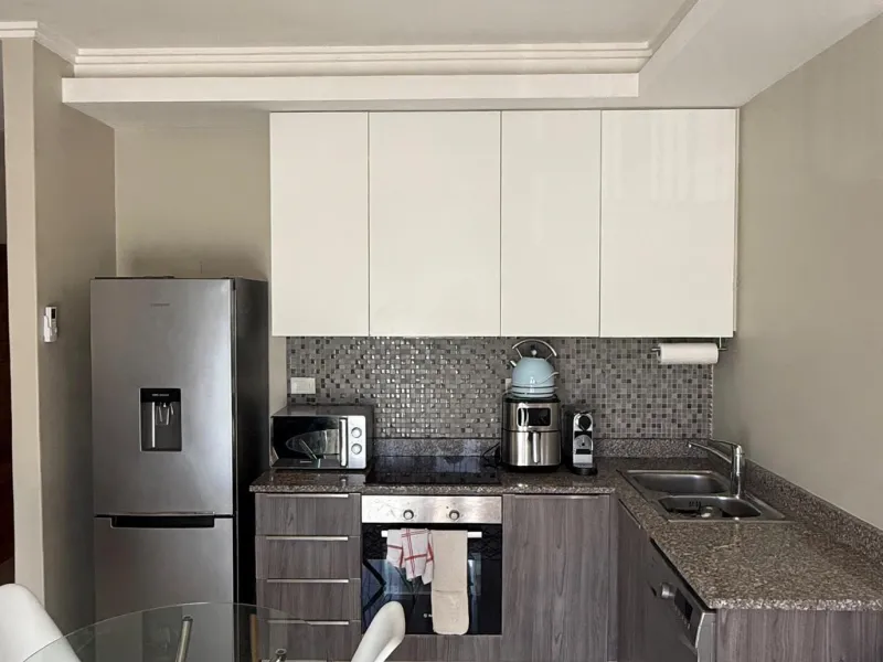 A functional kitchen featuring modern two-tone cabinetry, granite countertops, a mosaic tile backsplash, and integrated stainless steel appliances.