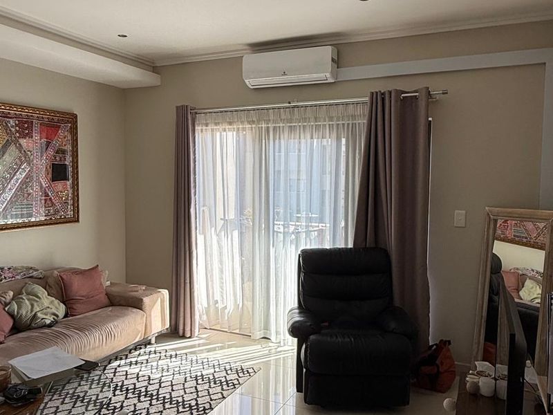 A well-lit living room featuring polished tiled flooring, a wall-mounted air conditioning unit, and sliding glass doors leading to an outdoor area.