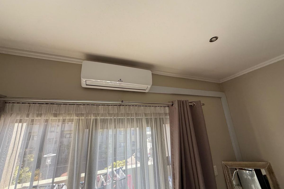A bedroom interior featuring a wall-mounted split-system air conditioning unit and recessed ceiling lighting.