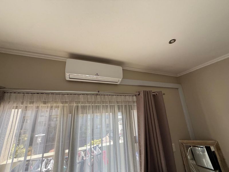 A bedroom interior featuring a wall-mounted split-system air conditioning unit and recessed ceiling lighting.