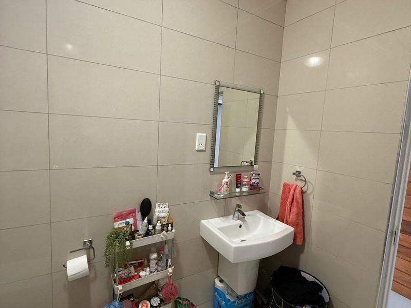 A functional bathroom featuring full-height ceramic wall tiling, a pedestal sink, and a wall-mounted mirror.