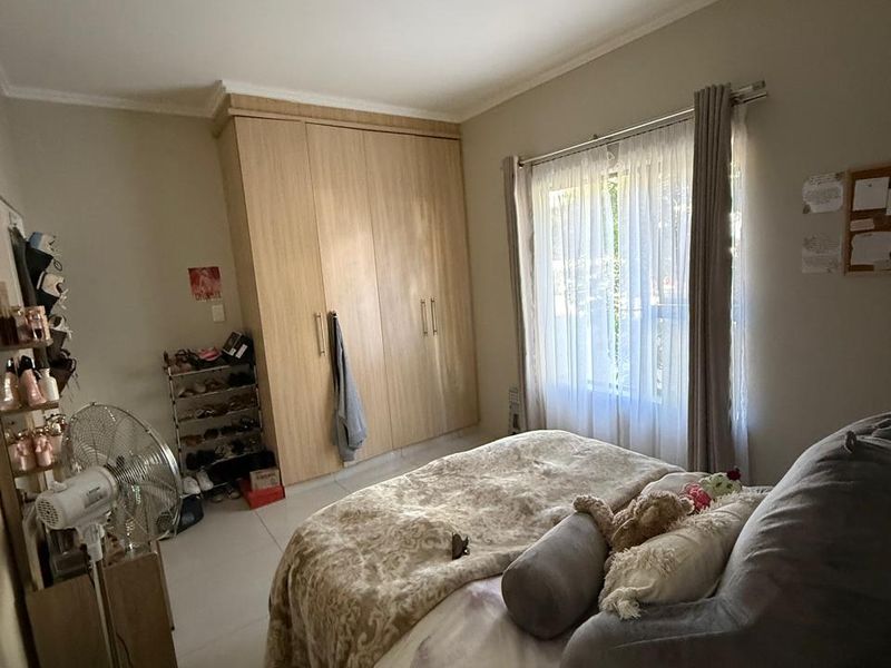 A functional bedroom featuring built-in wooden wardrobes, tiled flooring, and a window with curtain treatments, providing a neutral base for personalization.