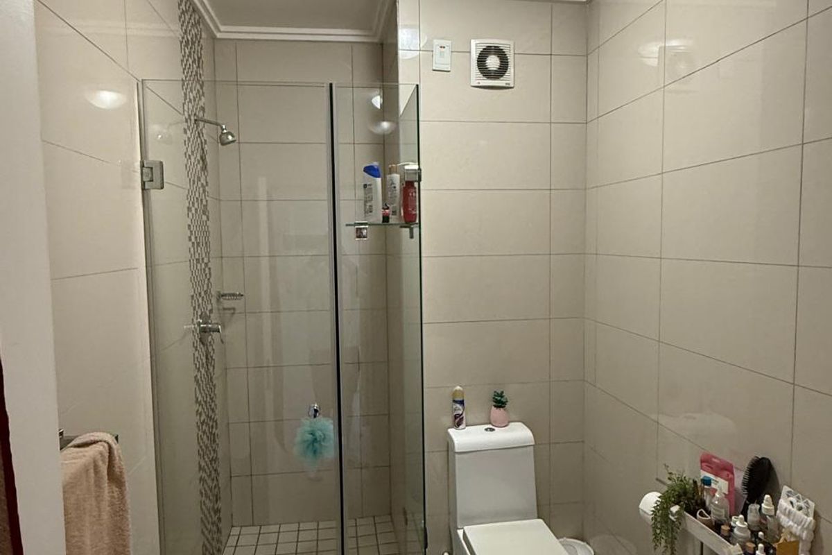 A functional bathroom featuring a glass-enclosed shower, modern toilet, and neutral wall tiling, providing a clean and practical space.