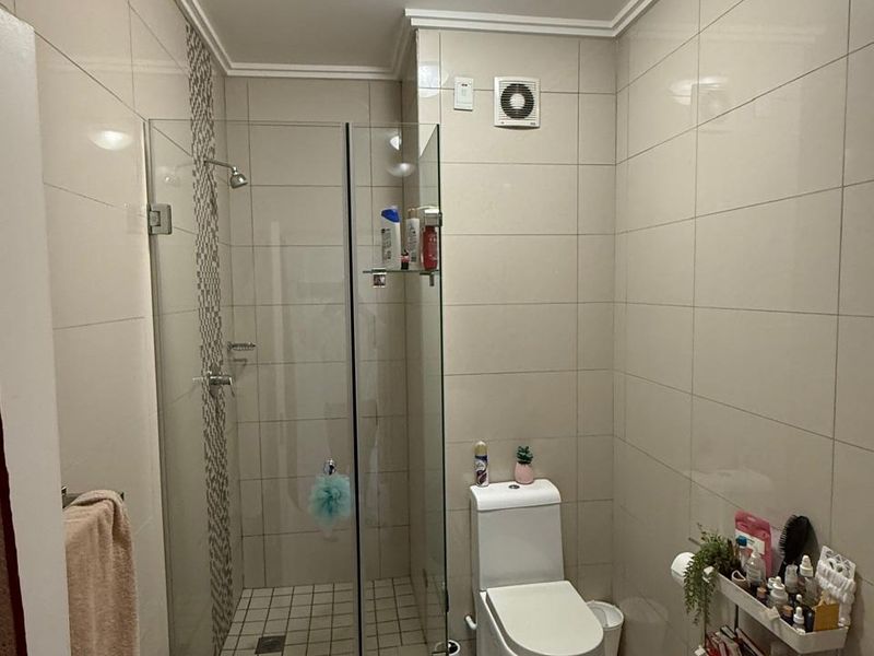 A functional bathroom featuring a glass-enclosed shower, modern toilet, and neutral wall tiling, providing a clean and practical space.