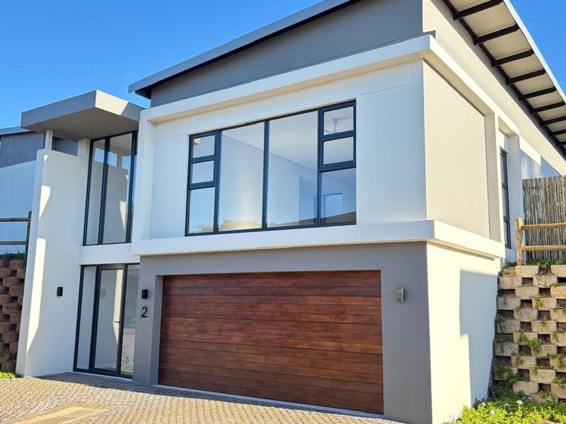 Modern double-storey townhouse featuring a contemporary facade, timber-look garage door, large aluminium windows, and a paved driveway with integrated retaining walls.