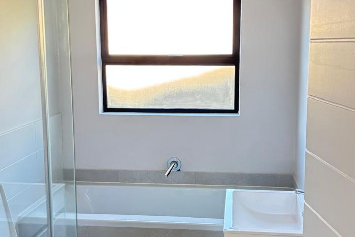 Modern bathroom featuring a built-in bathtub, wall-hung toilet, wall-mounted basin, and a glass-enclosed shower with neutral floor-to-ceiling tiling.