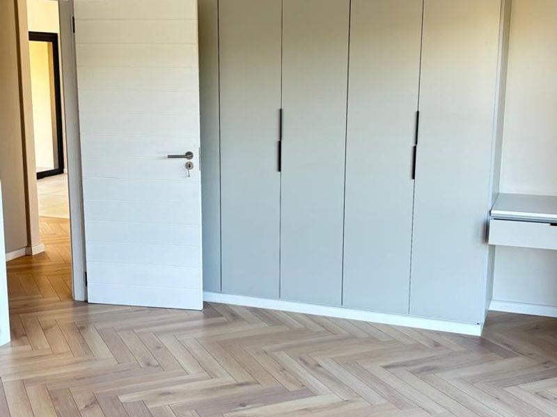 A bright, modern bedroom featuring high-quality herringbone timber flooring, extensive built-in cabinetry, and a sleek integrated vanity unit.