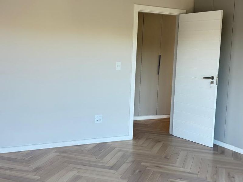 A bright, empty bedroom featuring modern herringbone timber flooring, neutral walls, and built-in cupboards, offering a clean and contemporary living space.