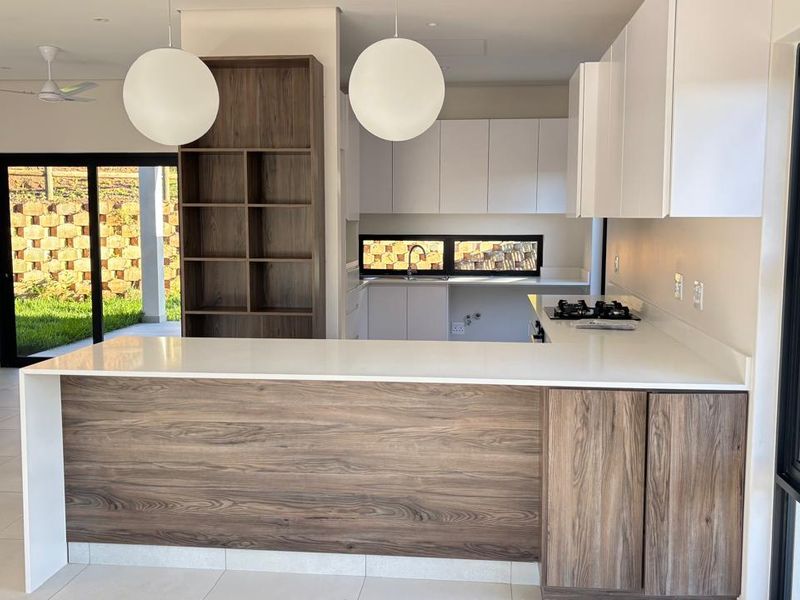 Modern kitchen featuring two-tone cabinetry, stone countertops, a gas hob, and built-in shelving, with direct access to the outdoor patio area.