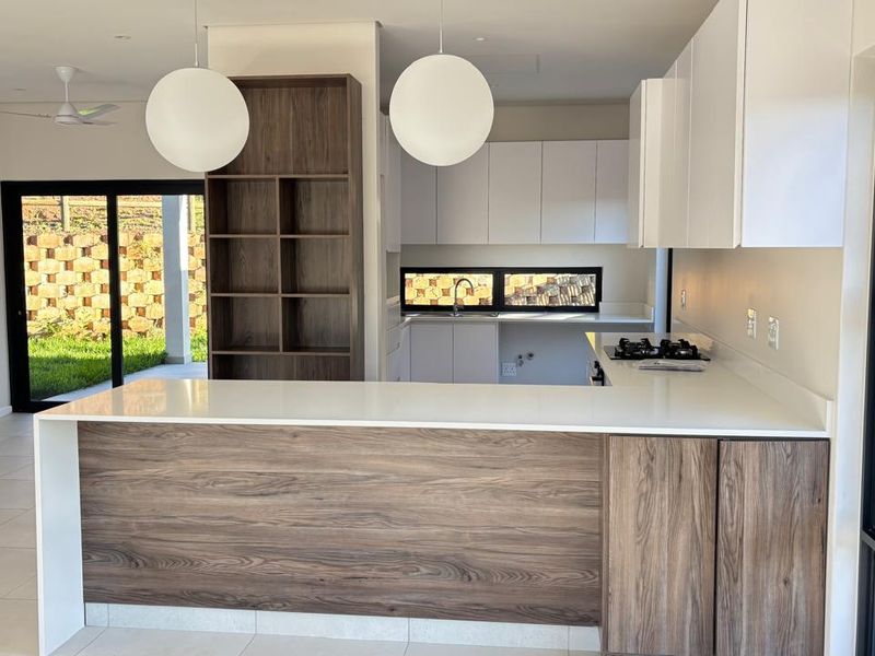 Modern open-plan kitchen featuring sleek two-tone cabinetry, stone countertops, gas hob, and seamless flow to the outdoor patio area.