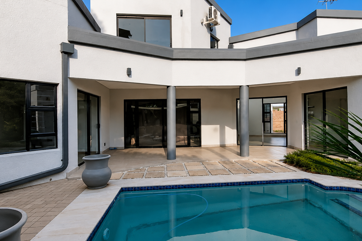 Rear exterior view featuring a modern swimming pool, paved deck area, and a covered patio with structural columns and large sliding glass doors.