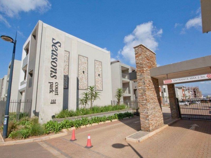 Front entrance view of Seasons Park Court apartment complex, featuring a secure gated access point, stone-clad pillars, and modern concrete building architecture.