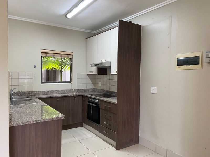 A functional kitchen featuring granite countertops, built-in cabinetry, an integrated oven and hob, and tiled flooring in a clean, vacant space.