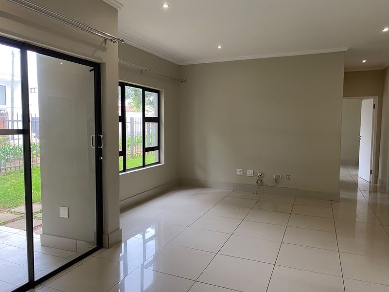 A bright, empty living area featuring large format floor tiles, recessed downlights, and a sliding glass door providing access to the exterior.