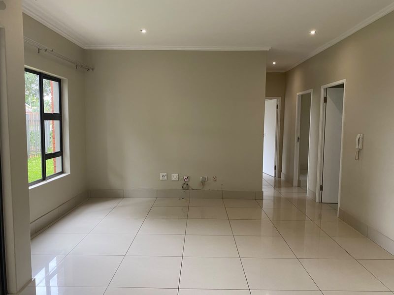 A bright, empty living room featuring neutral tiled flooring, recessed downlighting, and an intercom system, providing a clean canvas for interior design.