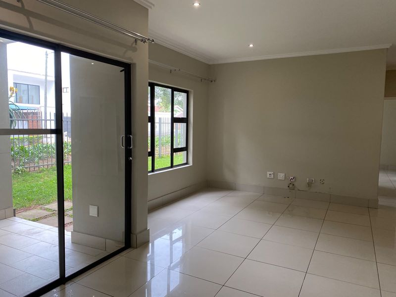 A bright, empty living area featuring neutral tiled flooring, recessed lighting, and large sliding glass doors providing access to the outdoor space.