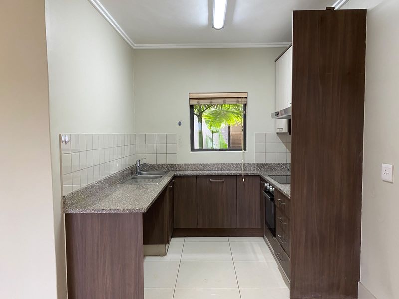 A clean, functional kitchen featuring dark wood cabinetry, granite countertops, built-in oven, hob, and extractor fan with neutral tiled flooring.