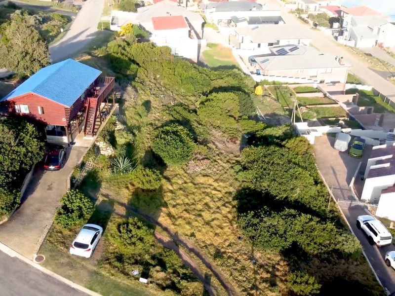 Aerial view of a residential vacant land plot situated in a developed neighborhood, featuring established vegetation and access to a paved driveway.