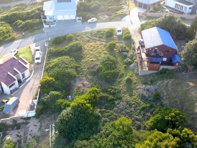 Aerial view of a vacant residential plot surrounded by established homes and natural vegetation in a coastal neighborhood.