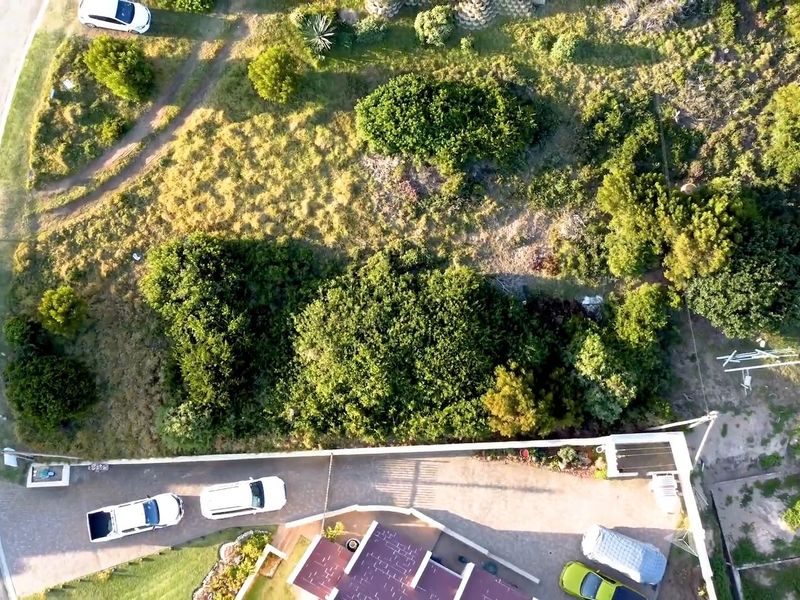 Aerial view of a residential vacant land plot featuring established vegetation, a paved driveway, and boundary walling.