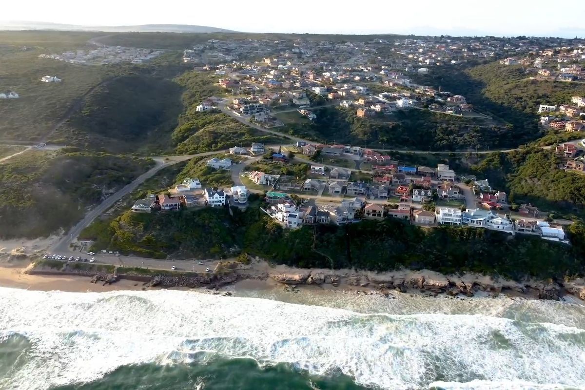 An aerial view of a coastal residential neighborhood situated along the shoreline, showcasing the surrounding landscape and proximity to the ocean.