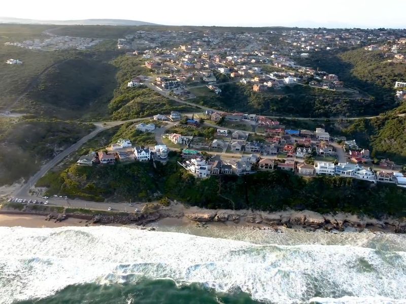 An aerial view of a coastal residential neighborhood situated along the shoreline, showcasing the surrounding landscape and proximity to the ocean.