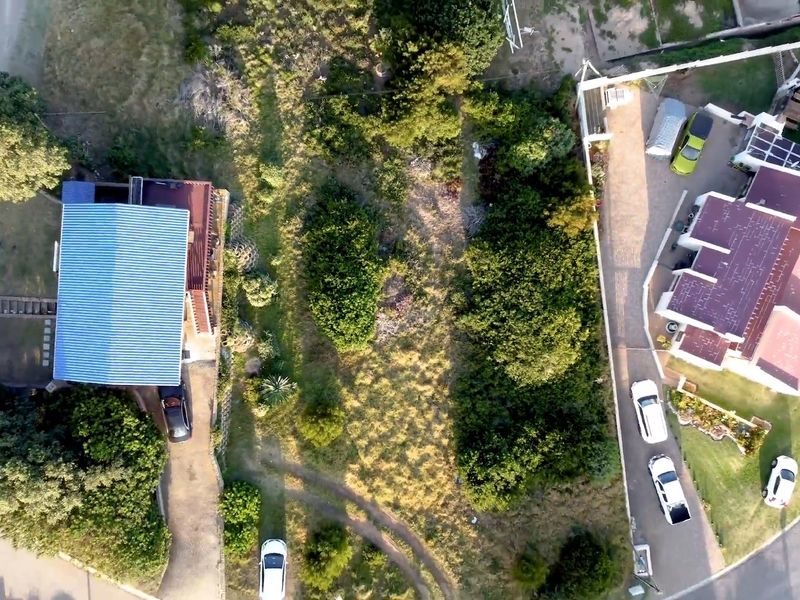 Aerial view of a residential vacant land plot situated between existing properties, featuring established vegetation and access to a paved driveway.