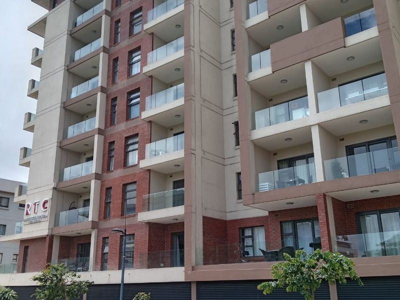 A modern multi-story apartment building featuring brick and concrete facade elements with glass-fronted balconies and integrated exterior lighting.