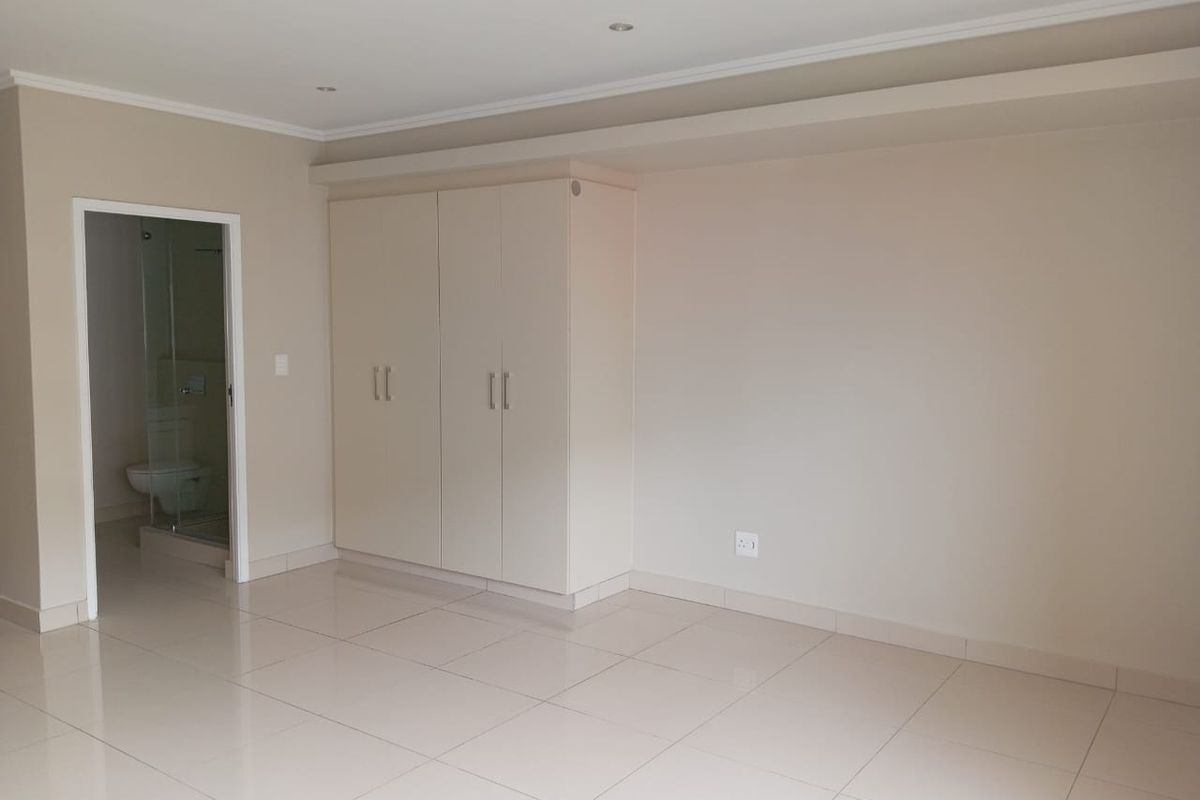 A bright, empty bedroom featuring neutral tiled flooring, built-in cupboards, and an adjoining en-suite bathroom.