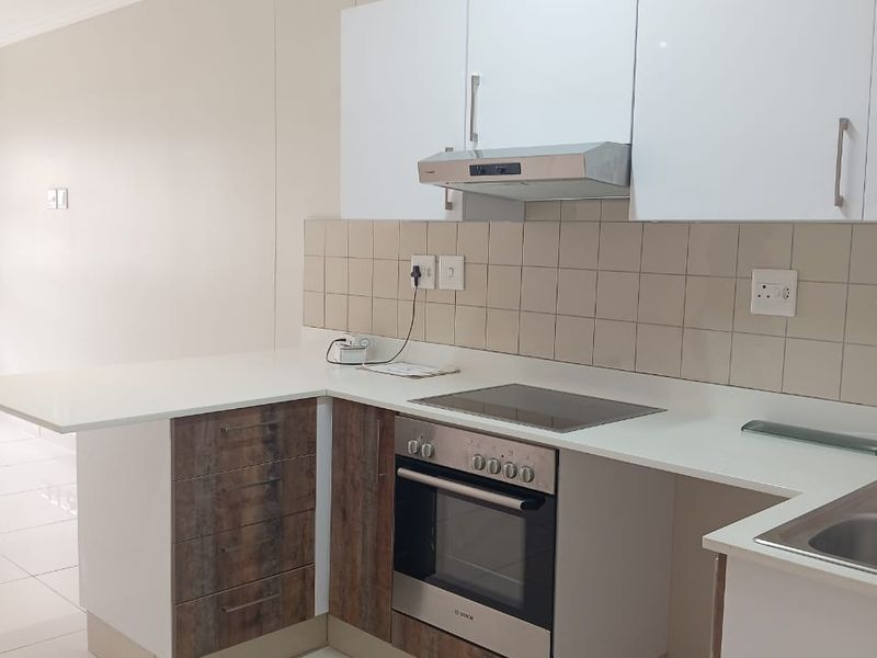 Modern kitchen featuring white gloss cabinetry, wood-grain accents, stone countertops, integrated oven, hob, and extractor fan with neutral tiled flooring.