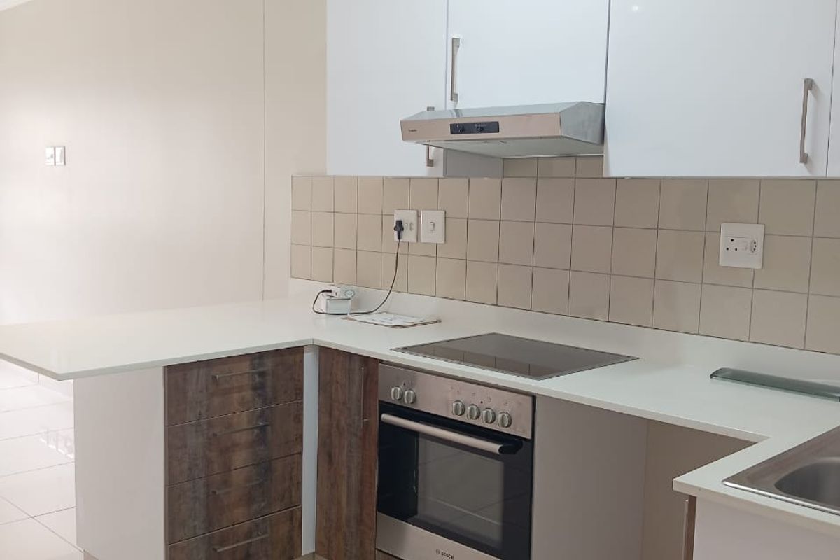 Modern kitchen featuring white gloss cabinetry, wood-grain accents, stone countertops, integrated oven, hob, and extractor fan with neutral tiled flooring.