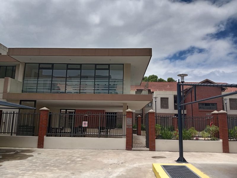 Front exterior view of the apartment complex featuring modern architecture, large glass windows, brick accents, and secure perimeter fencing.