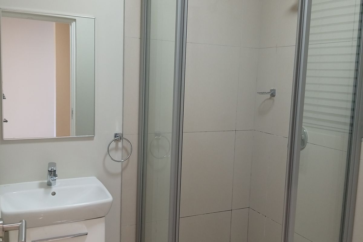 A clean, modern bathroom featuring a glass-enclosed shower, a vanity basin with storage, and neutral wall and floor tiling.