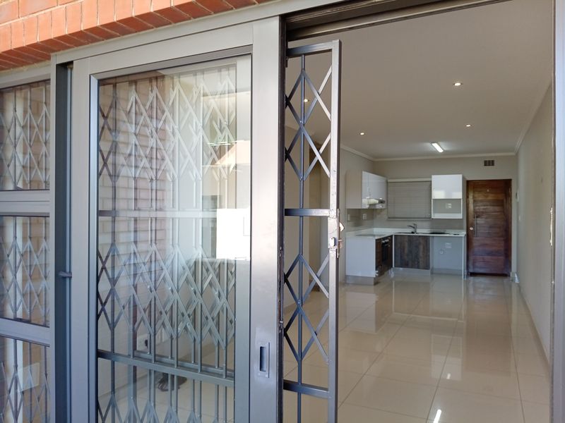 Open-plan living area featuring polished floor tiles, recessed lighting, and a modern kitchen with built-in cabinetry, accessible via a secure sliding gate.