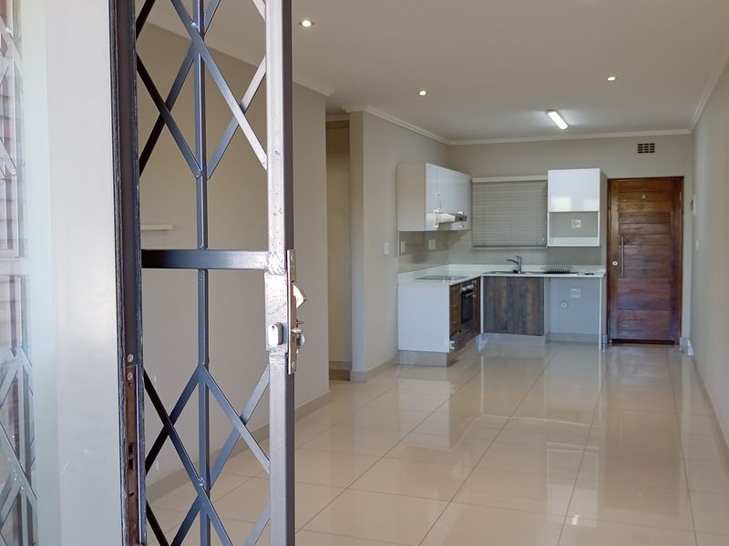 An open-plan living and kitchen area featuring polished porcelain tiles, modern cabinetry, built-in appliances, and a secure entrance.