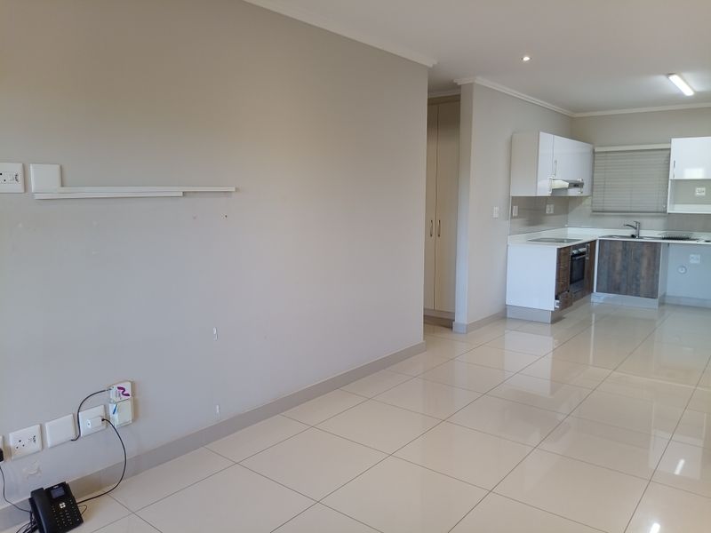 An open-plan living and kitchen area featuring neutral tiled flooring, modern built-in cabinetry, and integrated kitchen appliances in a clean, vacant space.