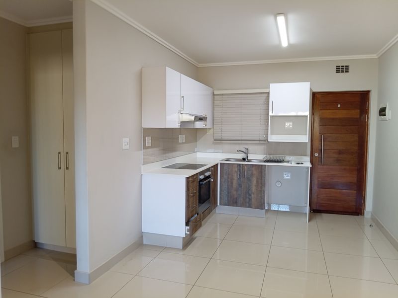 Modern kitchen featuring white and wood-tone cabinetry, integrated electric hob and oven, stainless steel sink, and neutral tiled flooring in an open-plan layout.
