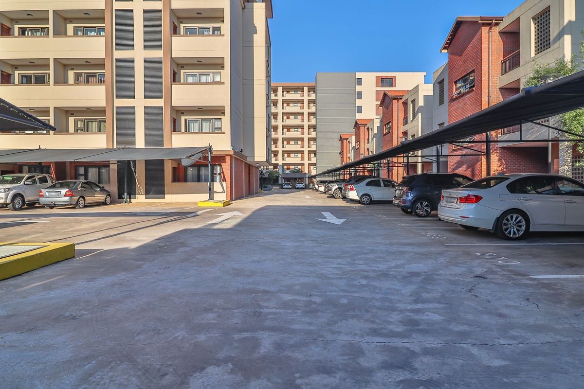 Exterior view of an apartment complex parking area featuring covered parking bays and paved driveway access.