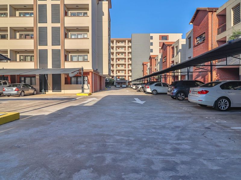 Exterior view of an apartment complex parking area featuring covered parking bays and paved driveway access.