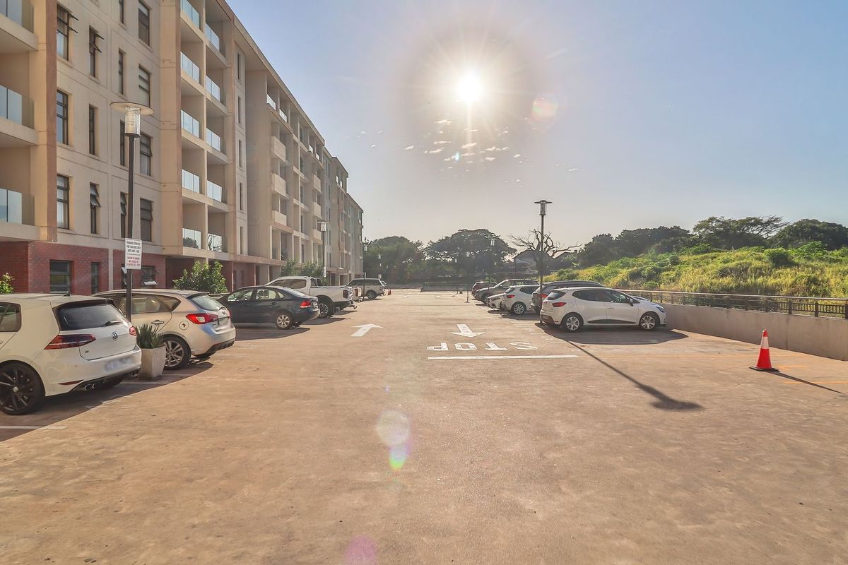An outdoor parking area adjacent to a modern apartment building with glass balcony railings and paved surfaces.