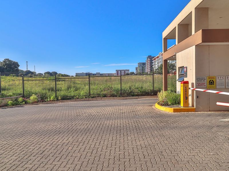 The property entrance features a paved driveway, a secure boom gate system, and perimeter fencing, providing controlled access to the apartment complex.